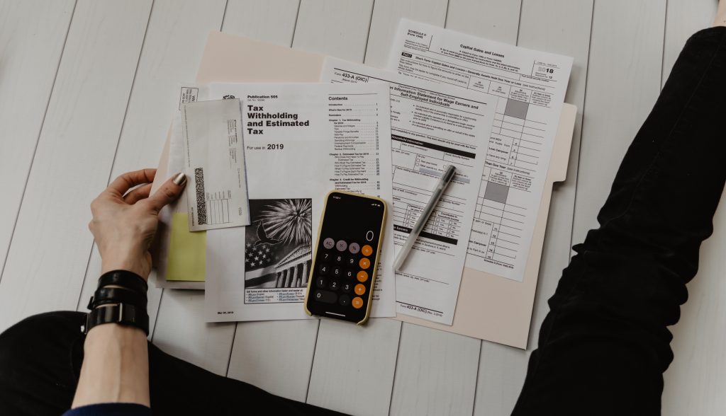 Cette image montre une femme tenant des fiches d'impôts des États-Unis, rédigées en anglais, ainsi qu'une calculette et un stylo. Elle semble concentrée sur la tâche complexe de la traduction financière, utilisant ses compétences linguistiques et mathématiques pour traduire les termes financiers et fiscaux en français. Les fiches d'impôts en anglais sur le bureau représentent le défi de la traduction financière transfrontalière, nécessitant une compréhension approfondie des systèmes fiscaux et financiers de différents pays. La femme utilise la calculette pour effectuer des calculs complexes et s'assurer que les chiffres sont corrects dans les traductions.